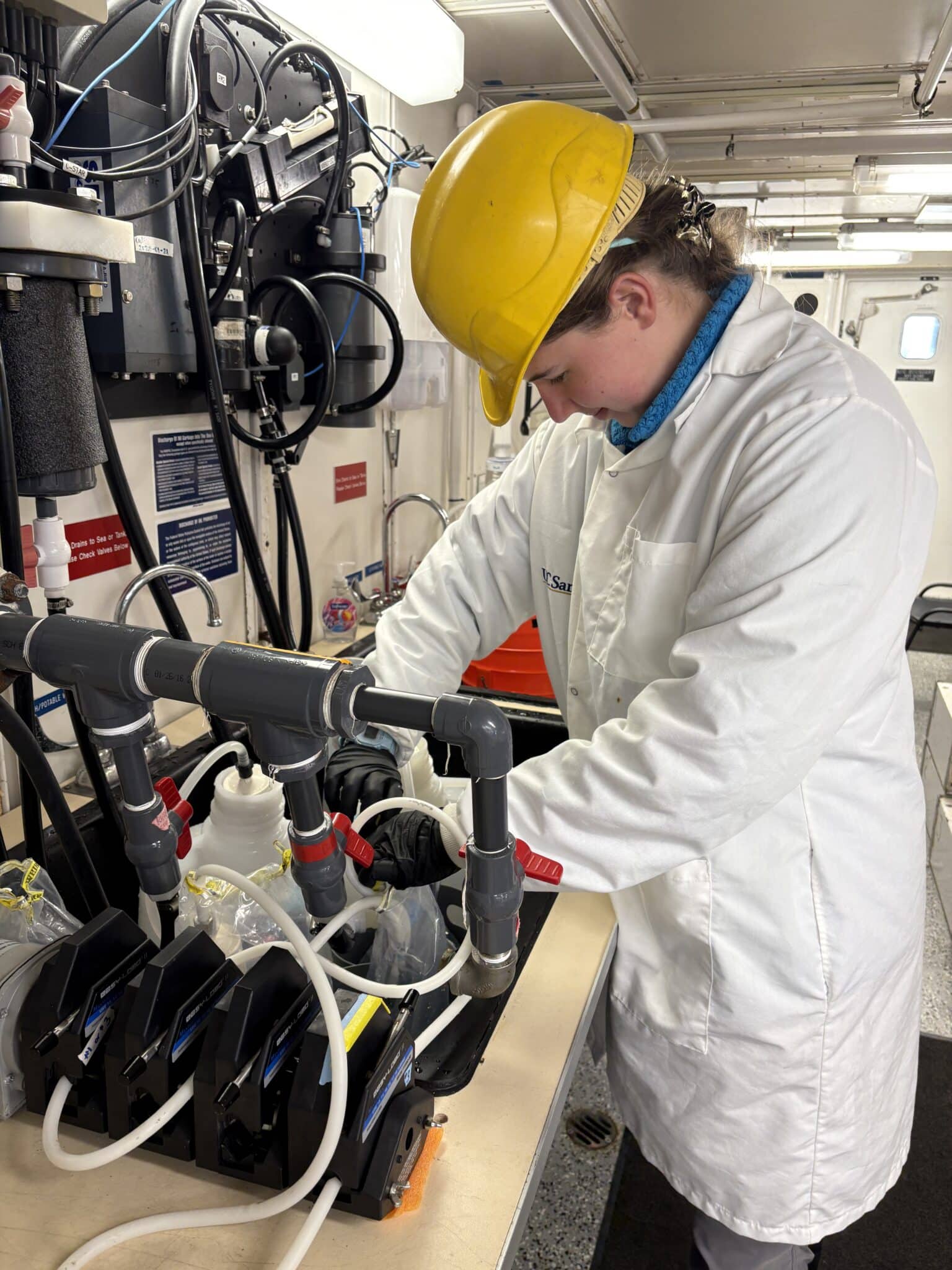 A picture of me in a hard hat in a lab in a ship
      working at a sink.