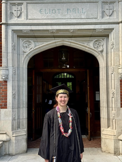 Me in a graduation robe and cap in front of a building arch that says
      'ELIOT HALL' on it