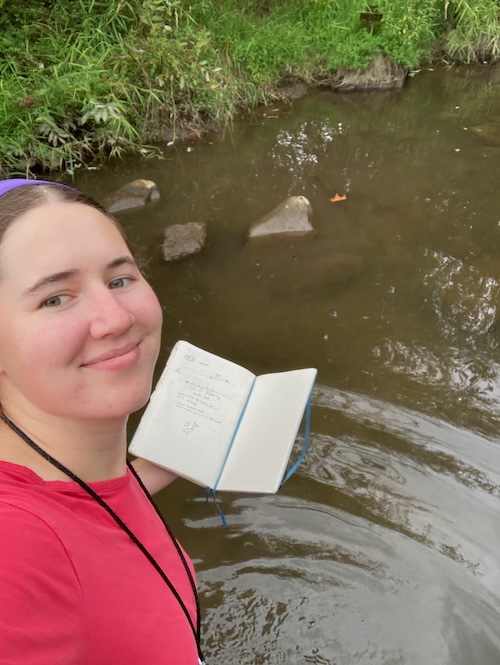 Me standing in a river holding a notebook and smiling