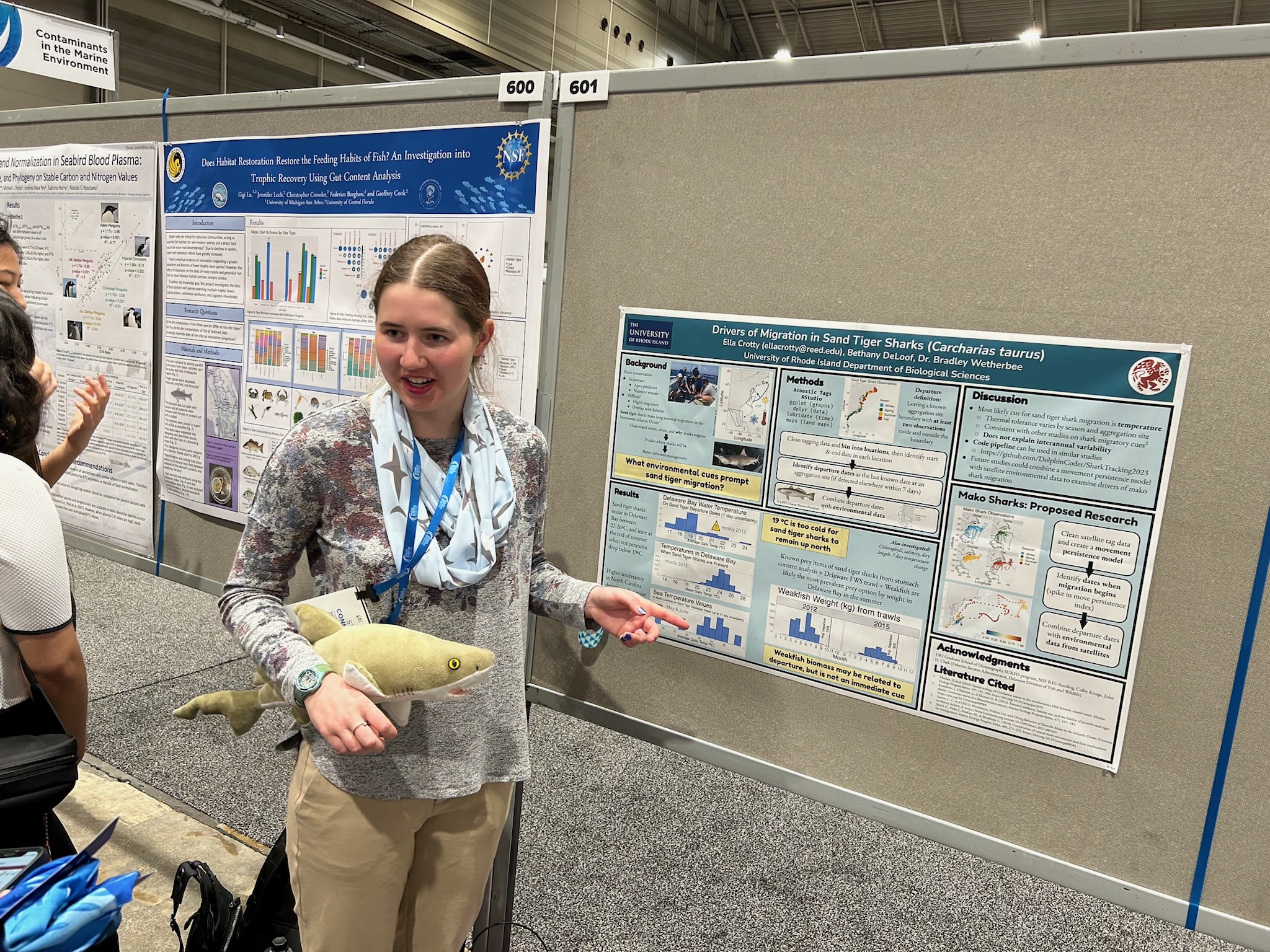 Me presenting a poster at a conference, holding a stuffed animal shark.